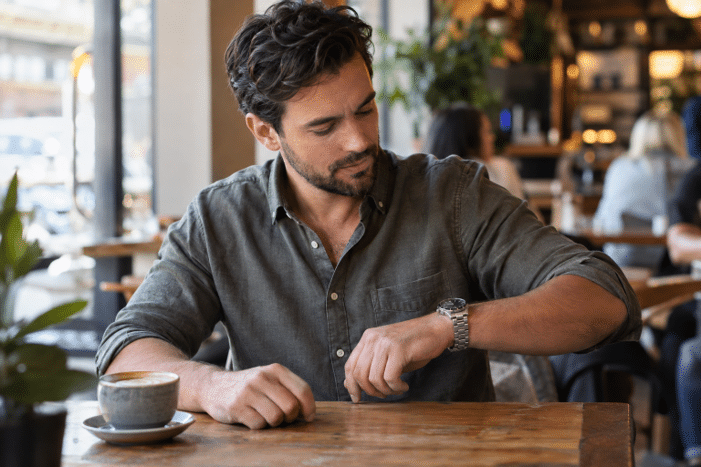 Man glancing at a steel wristwatch while sitting at a cafe table