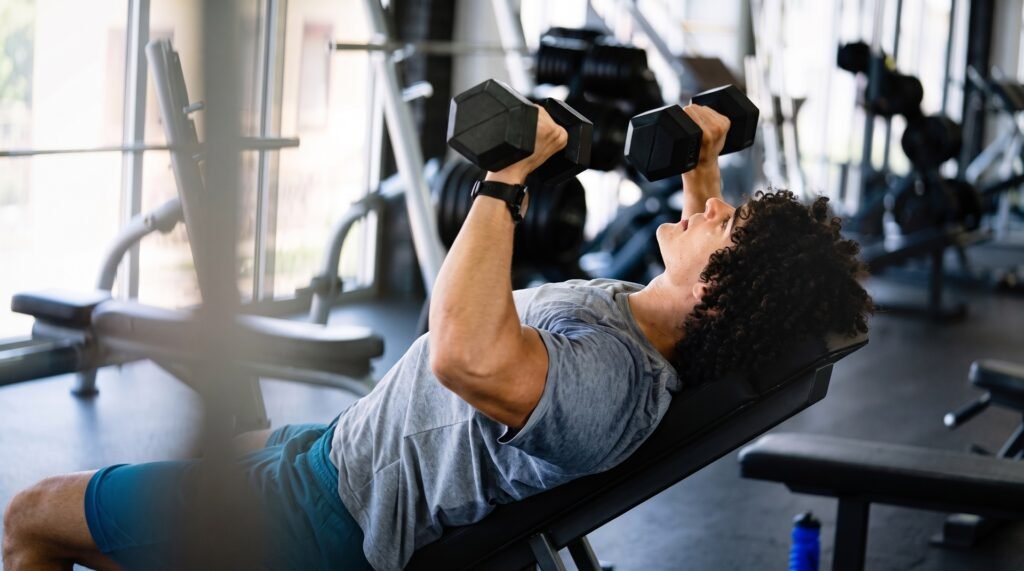 Man performing a dumbbell incline bench press in a gym