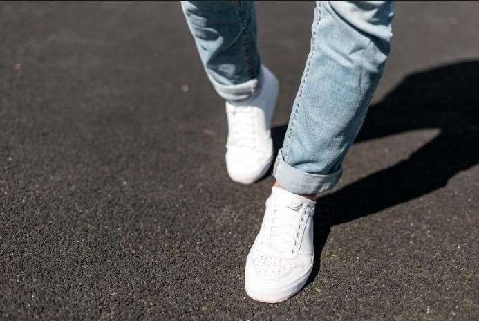 Man walking in light jeans and clean white leather sneakers on a city street