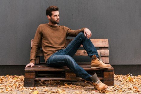Man seated, wearing brown sweater and dark denim jeans